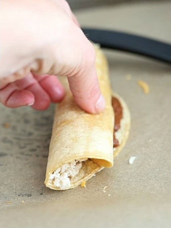 Rolled enchilada sealed with enchilada sauce placed seam side down.