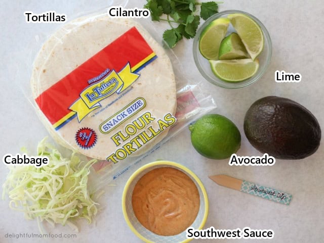 Labeled ingredients for cod fish tacos: tortillas, cilantro, lime, avocado, shredded cabbage and southwest sauce.