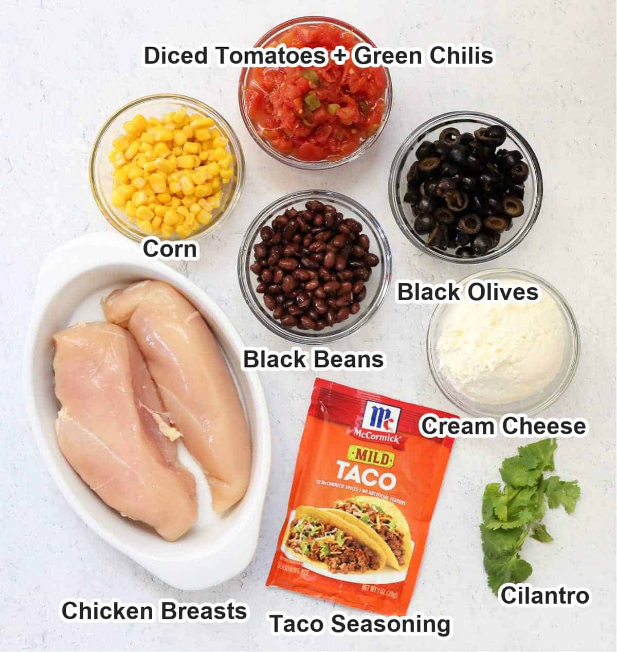 Labeled ingredients for crockpot taco chicken chili: chicken breasts, corn, diced tomatoes with green chilis, black beans, black olives, cream cheese, taco seasoning and cilantro.