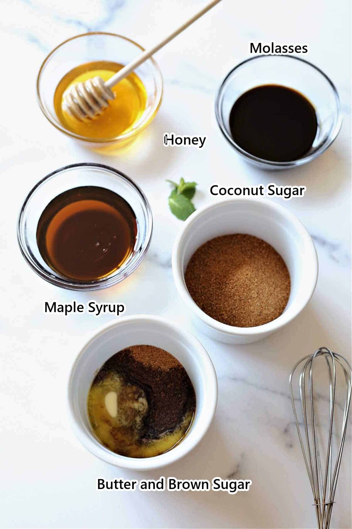 Labeled maple syrup substitutes: honey, molasses, maple syrup, coconut sugar, and butter with brown sugar in bowls with a whisk.