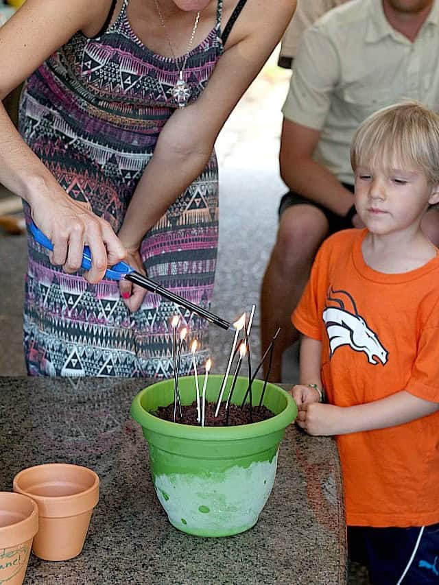 Lighting the candles on a gluten-free Oreo dirt cake in a green pot at a birthday party.