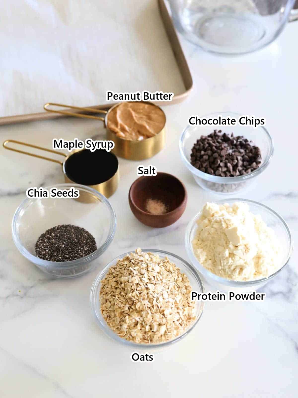 Labeled ingredients for no-bake protein balls: oats, protein powder, peanut butter, maple syrup, chia seeds, salt and chocolate chips.