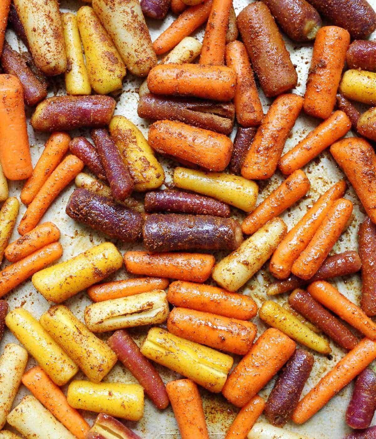 Seasoned rainbow carrots spread in one layer on a baking pan ready to roast.
