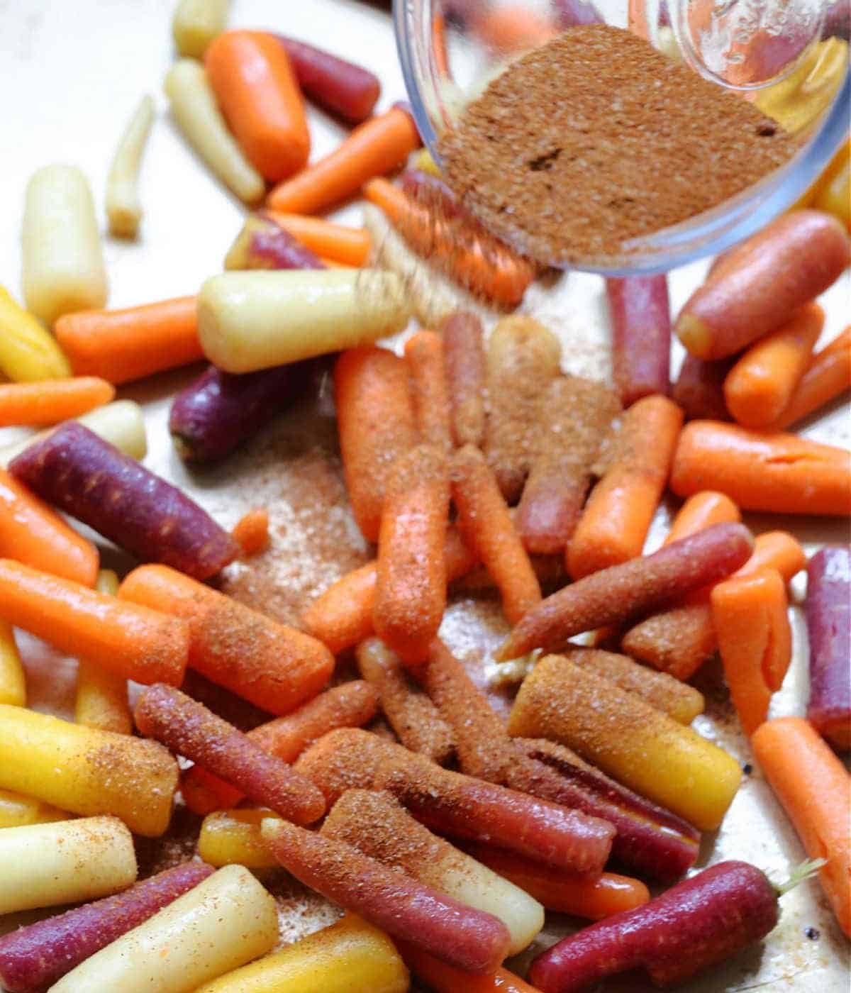 Turmeric paprika seasoning mix being sprinkled over rainbow carrots.