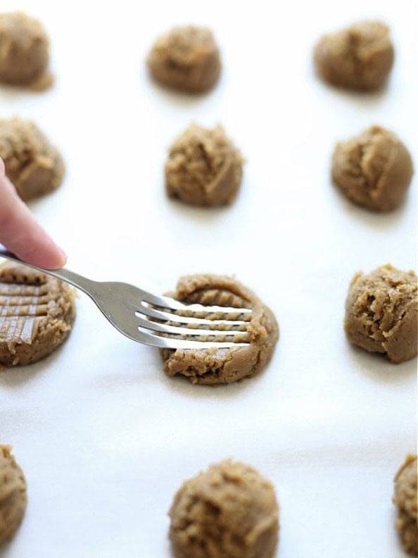 Back of a fork pressing a crisscross pattern into a ball of sunbutter cookie dough on the baking sheet.