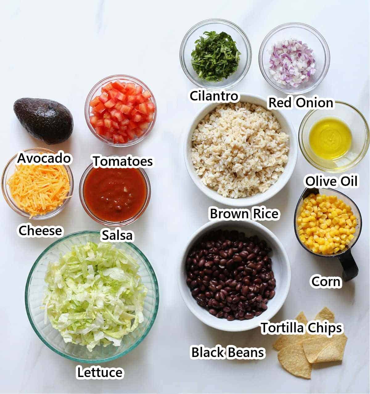 Labeled ingredients for vegetarian taco salad including black beans, brown rice, salsa, tomatoes, lettuce, cheese, corn, cilantro, red onion, avocado, olive oil and tortilla chips.
