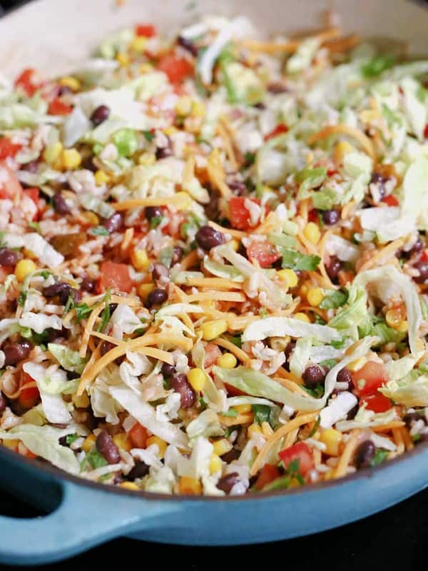 Warmed black bean taco salad mixed with lettuce, salsa and cheese in a saute pan.