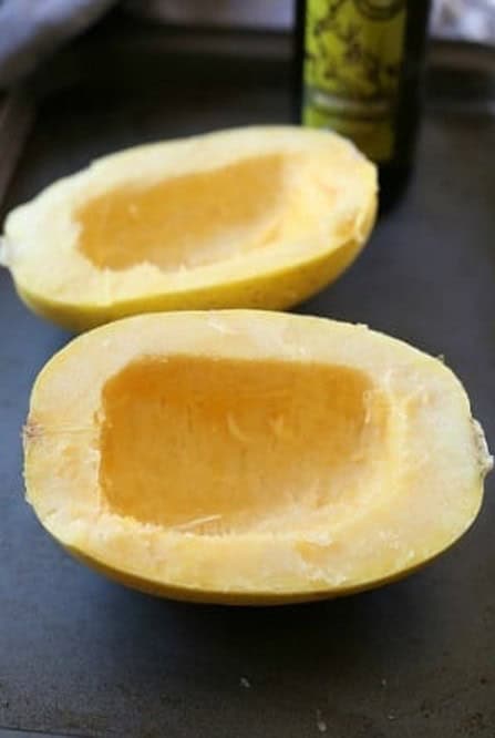 Spaghetti squash halves with the seeds scooped out on a baking sheet.
