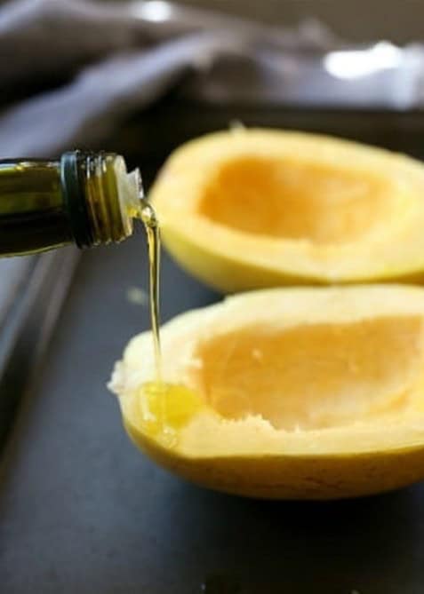Drizzling olive oil over halved spaghetti squash on a baking sheet.