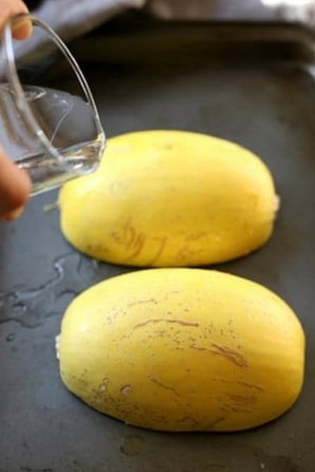 Pouring water onto a baking sheet with spaghetti squash halves placed face down.