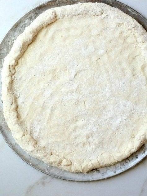 Pizza dough rolled out on a pizza pan.