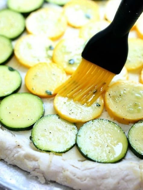 Basting the zucchini pizza with the olive oil dressing.